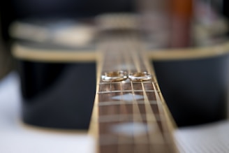 Two wedding rings rest on the fretboard of an acoustic guitar, creating a symbolic representation of love and harmony.