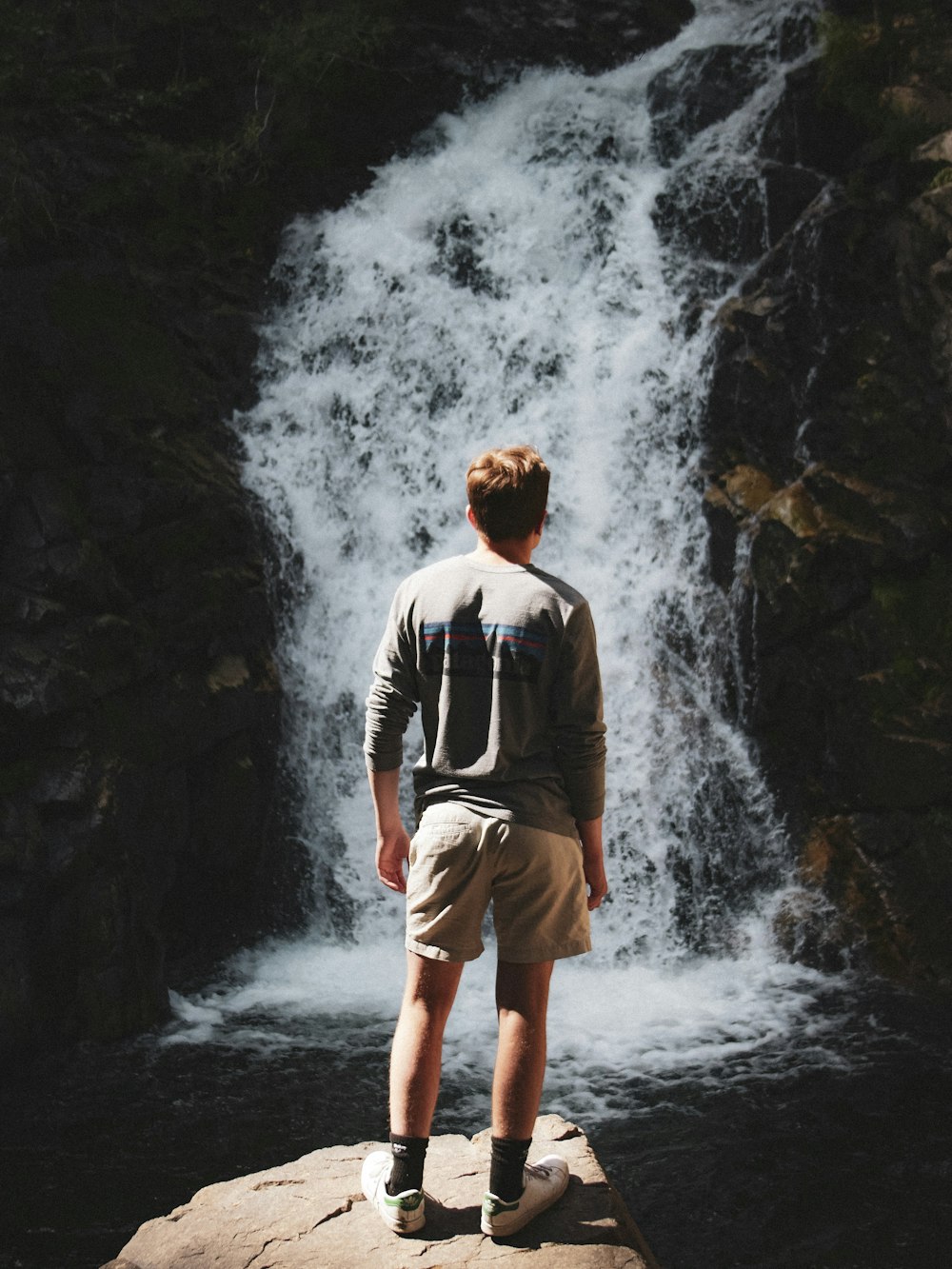 man standing on rock while facing waterfalls during daytime