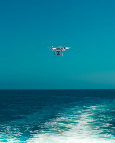 A sleek drone flying over a calm sea, capturing data from a fishing boat below.