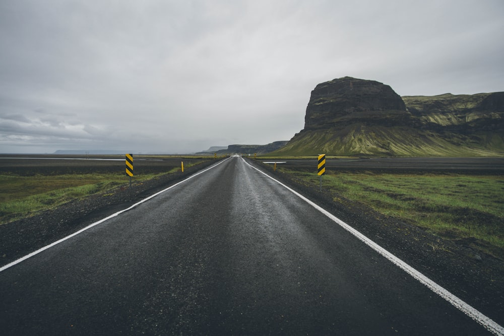 empty concrete road between green grass under gray sky