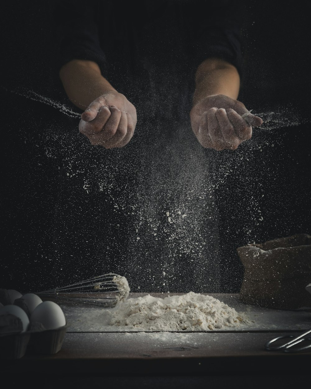 卵と泡立て器の横のテーブルに小麦粉を注ぐ人
