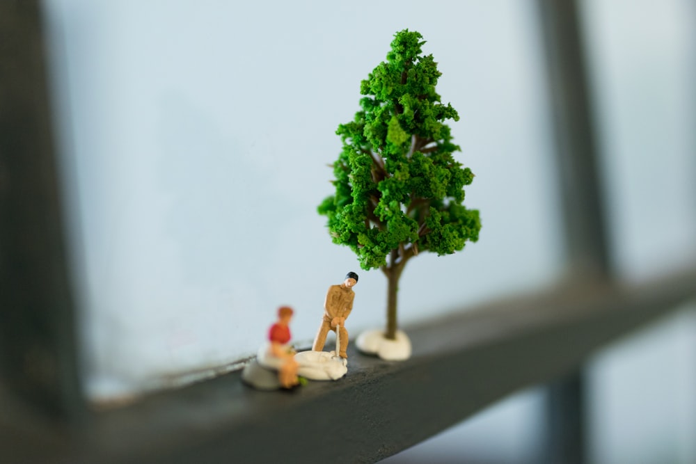 selective focus photography of two person figure beside green tree miniature on window