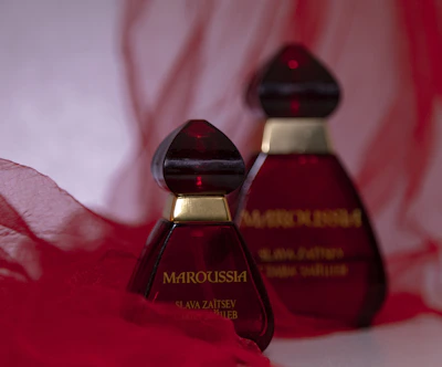 A sleek perfume bottle with a deep red hue against a silver backdrop.