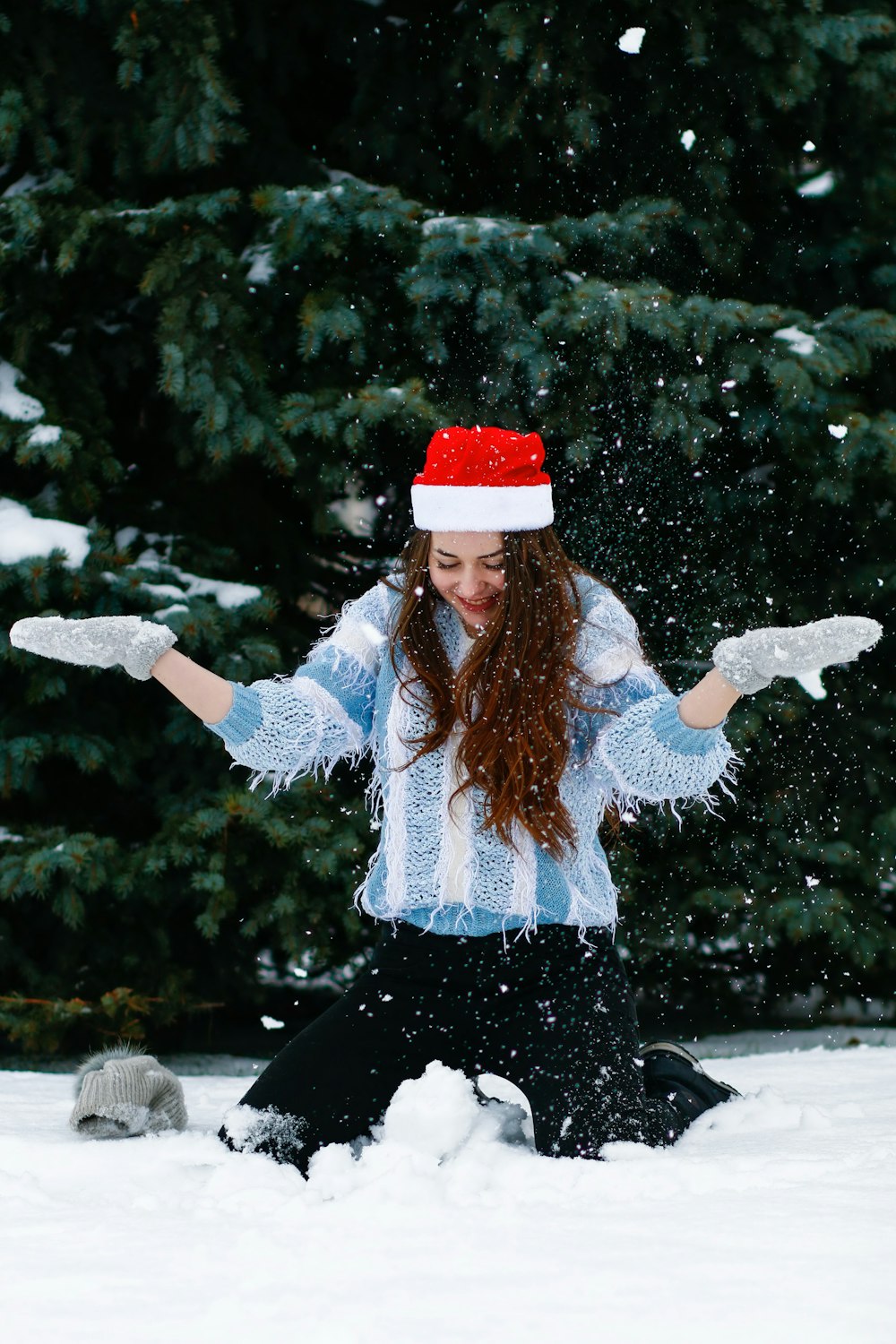 woman in blue sweater playing with white snow near green tree during daytime