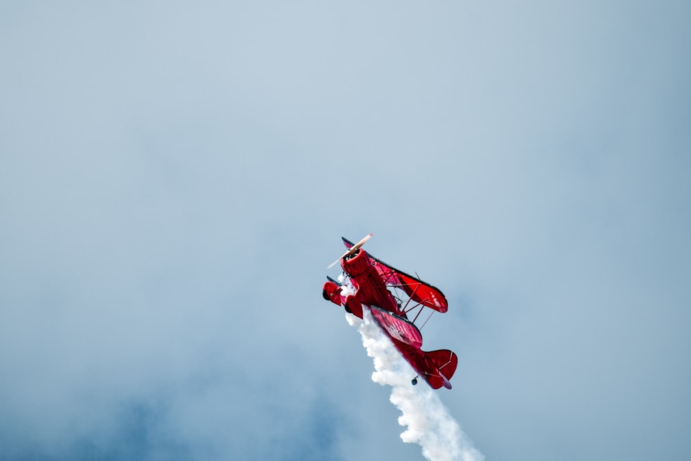 red exhibition plane releasing smoke during daytime
