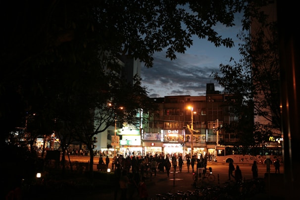 A bustling city street scene at dusk with glowing shop windows and people walking.