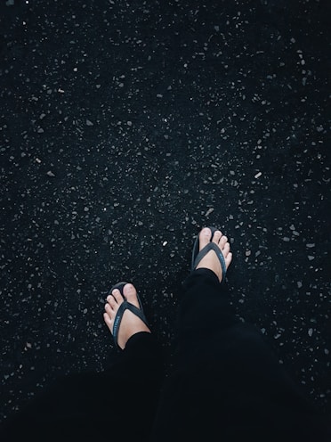person in black flip flops and black pants standing on black asphalt floor