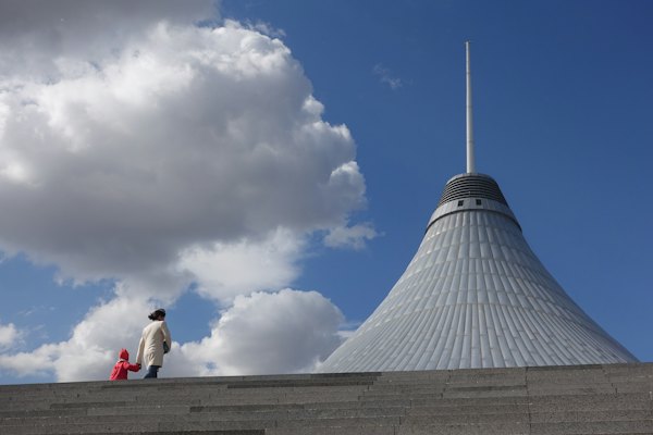 Woman and child walking beside gray concrete building — Astana, Kazakhstan