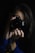 A person holding a camera up to their face, capturing an image. The scene is dimly lit, focusing on the camera and the person's hands. The background is dark, emphasizing the photographer's concentration.