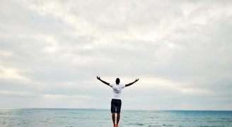 man raising hands standing near seashore during daytime