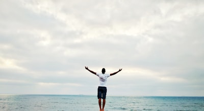 man raising hands standing near seashore during daytime