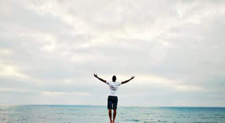 man raising hands standing near seashore during daytime
