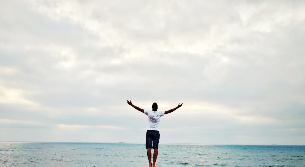 man raising hands standing near seashore during daytime