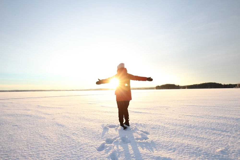 Person in Jacke, die während der goldenen Stunde auf Schnee steht