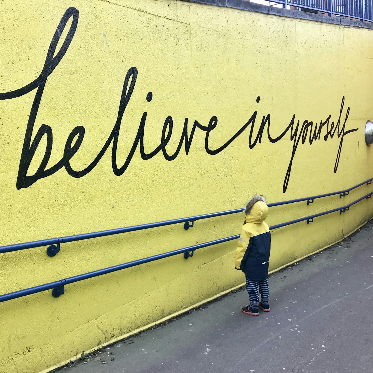 Child stands in front of a large wall that reads “Believe in yourself.” Self confidence quotes blog by inspired Idiots