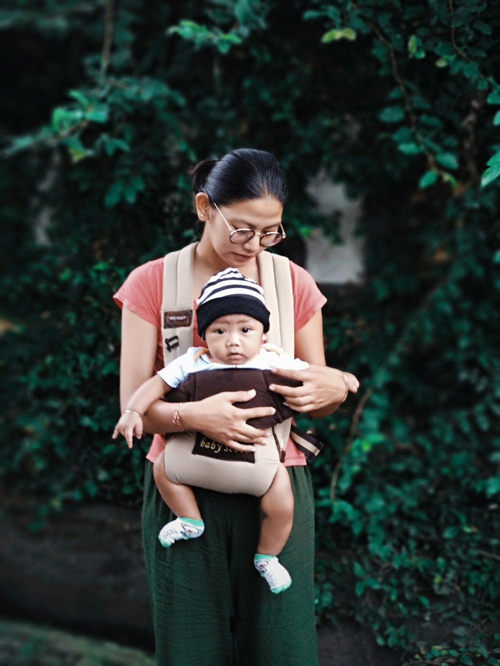 woman holding baby beside green plants