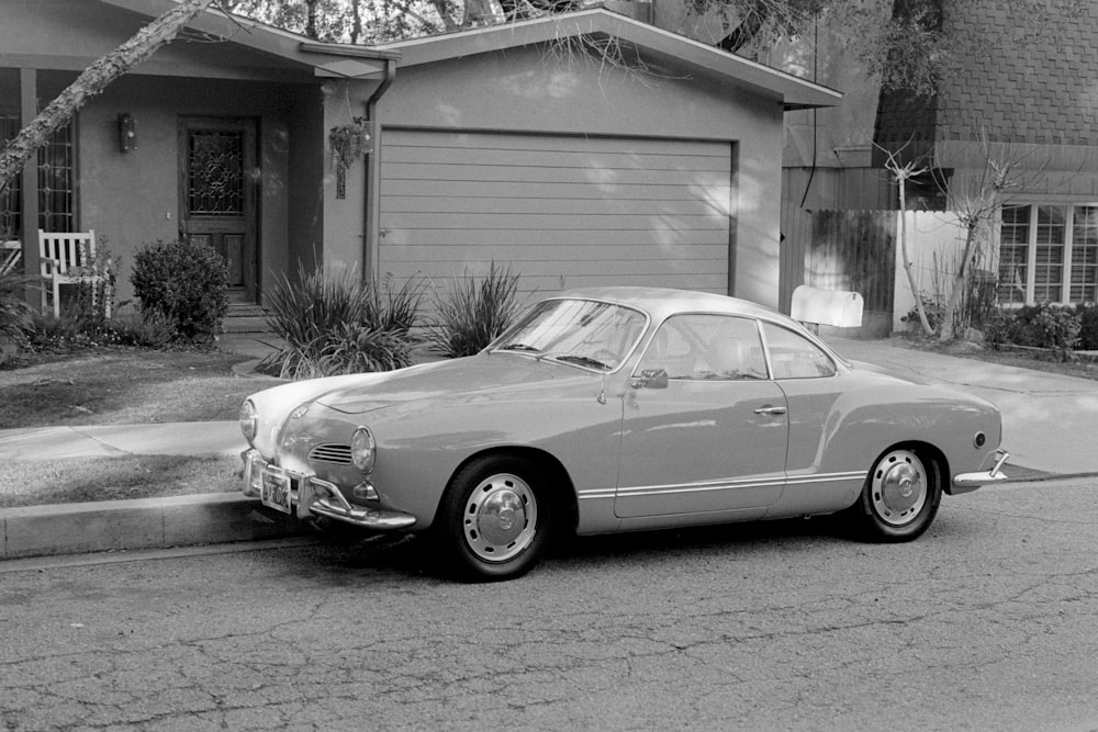 classic coupe park near house in grayscale photo