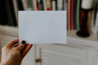 Close-up of a hand holding a finely detailed fake health insurance card on a wooden desk.