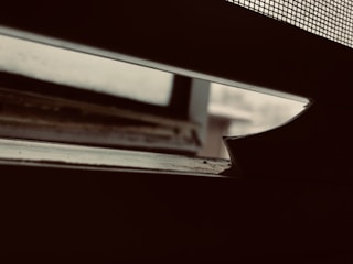 A close-up view of a partially open window, with a focus on the window sill and a wire mesh screen. The background appears blurry and overcast, creating a somber atmosphere with low lighting.