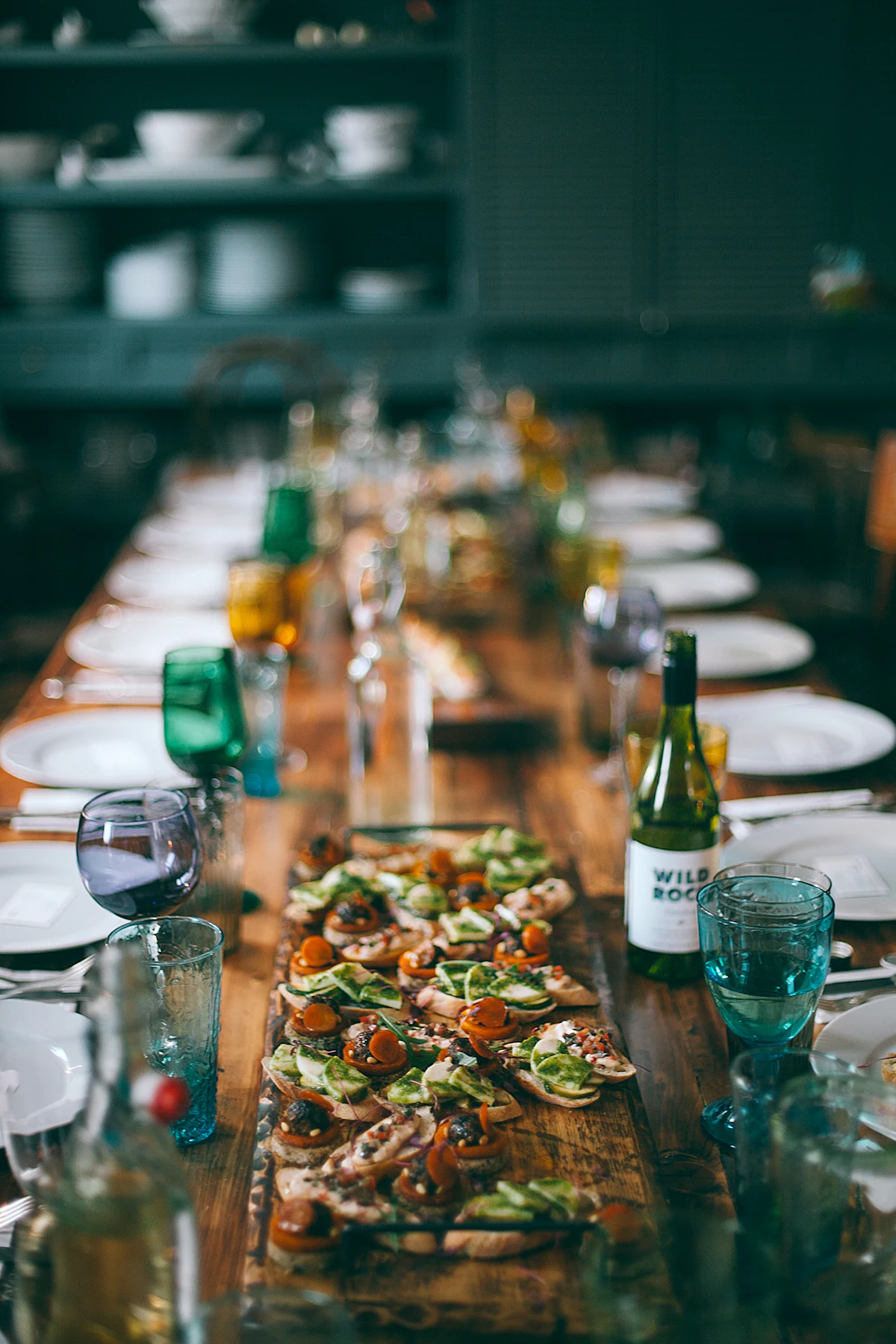 A long table laid end to end with shared plates, glasses and bottles, waiting for the party.
