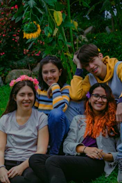 A group of young people sitting in a circle outdoors, surrounded by lush green hills and soft sunlight.