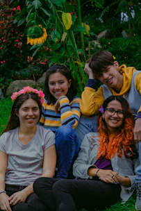 A group of young people sitting in a circle outdoors, surrounded by lush green hills and soft sunlight.