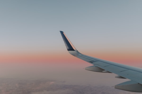 View from airplane window showing wing against sunset sky over clouds