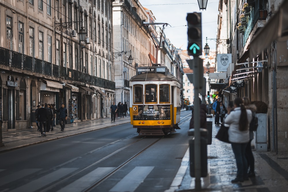 people standing on pathway in front of white and yellow tram on road during daytime