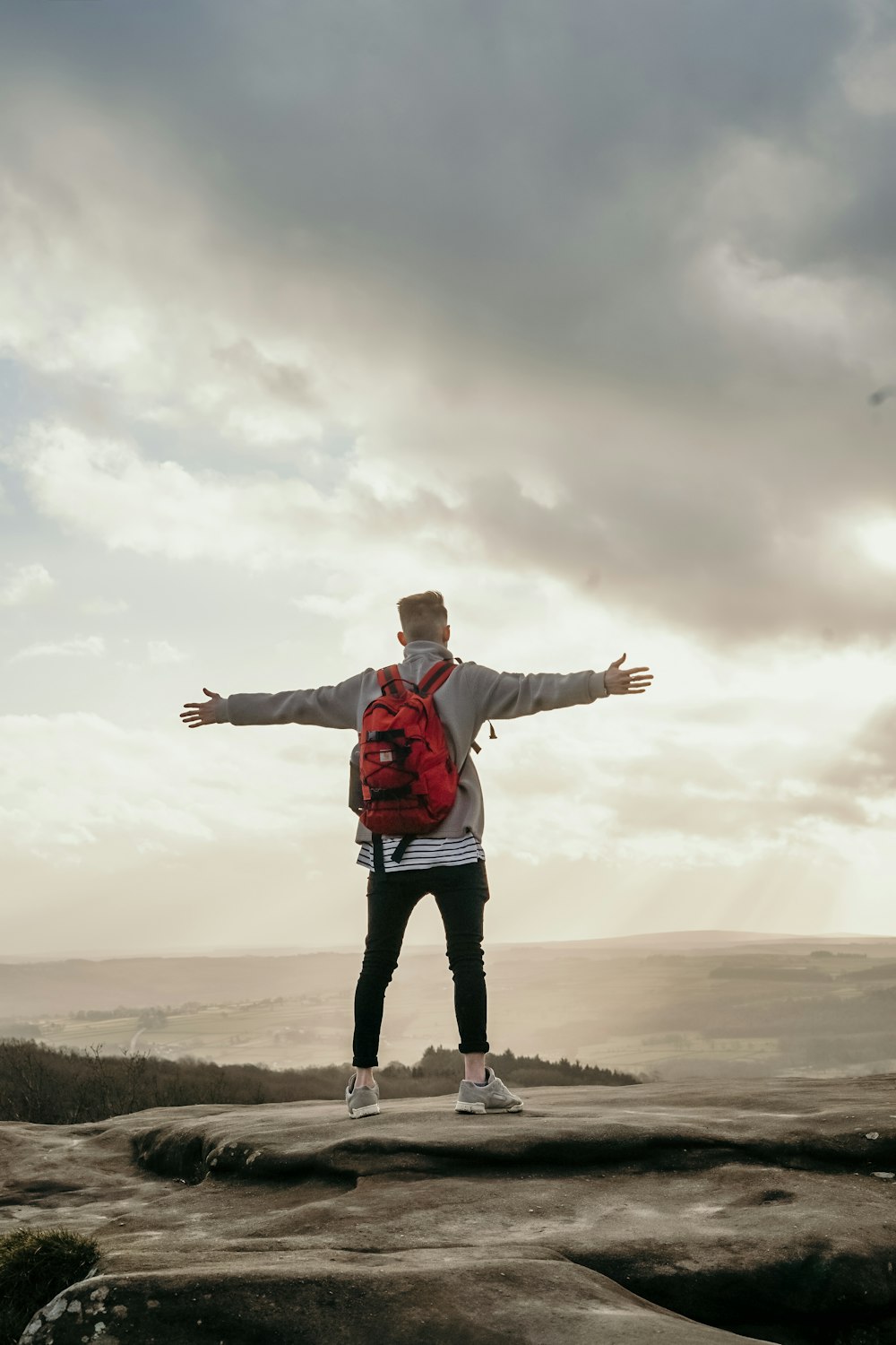 man spreading his arm wide while standing on top of hill