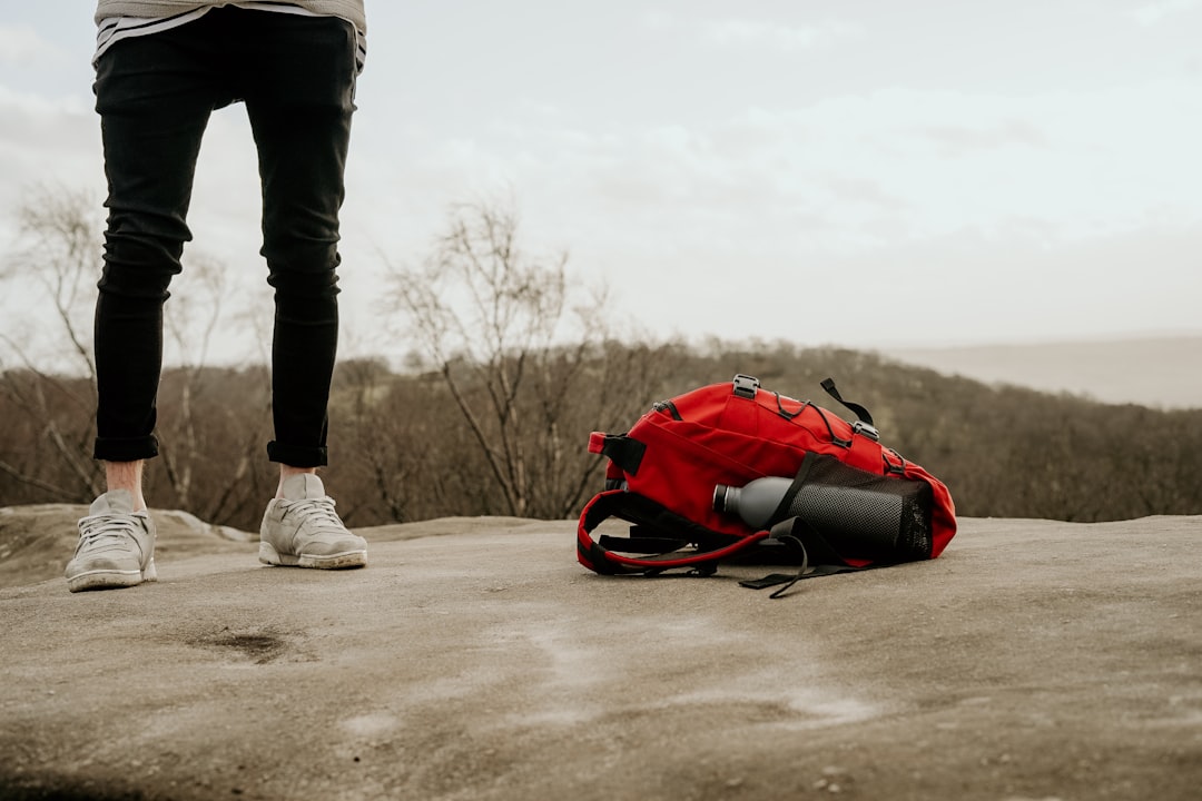 person standing beside red and black hiking backpack