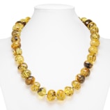 A necklace composed of large, round amber beads strung together, displayed on a white mannequin bust. The beads are polished and exhibit natural inclusions, giving them a unique and organic appearance with shades of yellow and brown.