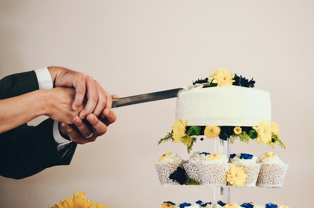 couple both holding knife slicing a cake on tray