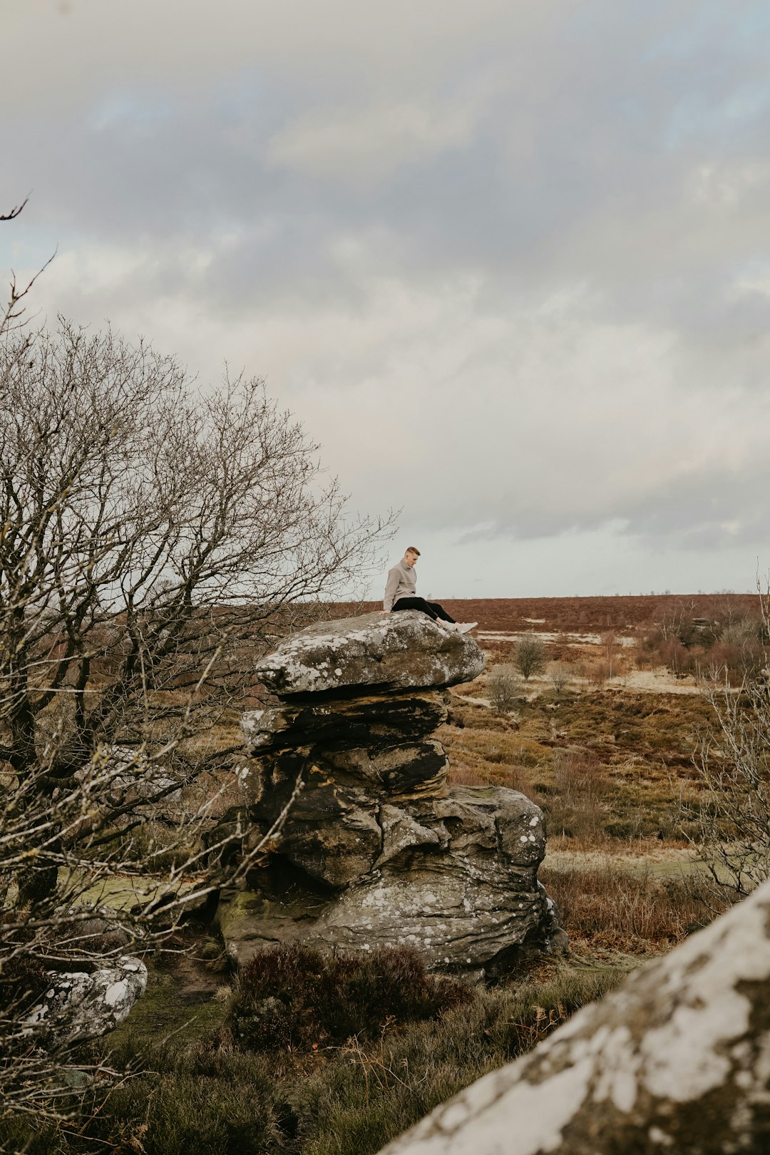 person on top of rock formation near bare trees under white skies