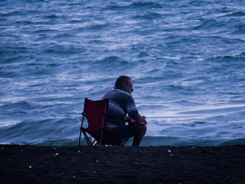 man sitting on camper chair watching waves