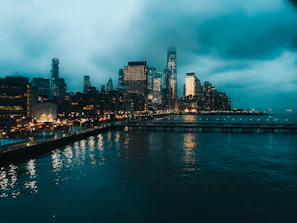 A moody, cinematic shot of a city skyline at dusk with glowing lights reflecting on water