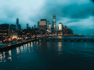 A moody, cinematic shot of a city skyline at dusk with glowing lights reflecting on water