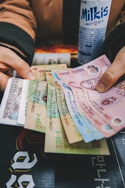 A person is holding a variety of Vietnamese banknotes spread out in their hands, with a can of Milkis beverage placed nearby.
