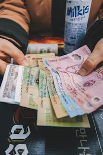 A person is holding a variety of Vietnamese banknotes spread out in their hands, with a can of Milkis beverage placed nearby.