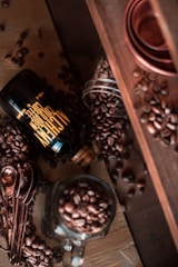 A close-up of a handcrafted crema bottle next to fresh vanilla beans and nutmeg, set against a rustic wooden background.