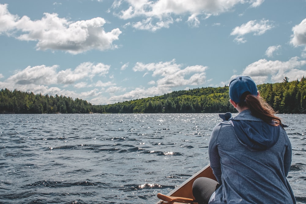 person wearing blue jacket sitting on wooden boat on the water with clear skies