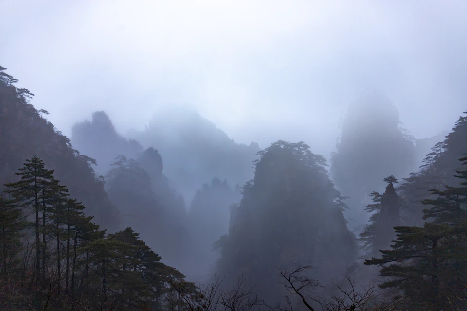 Foggy mountain range with dark green mountains and trees in misty, overcast conditions