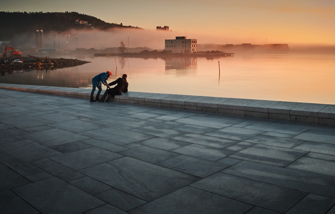 two person sitting on concrete floor near body of water during golden hour