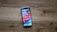 A smartphone with a colorful display full of app icons lies on a wooden surface. The screen shows various apps, including social media platforms, utilities, and games.