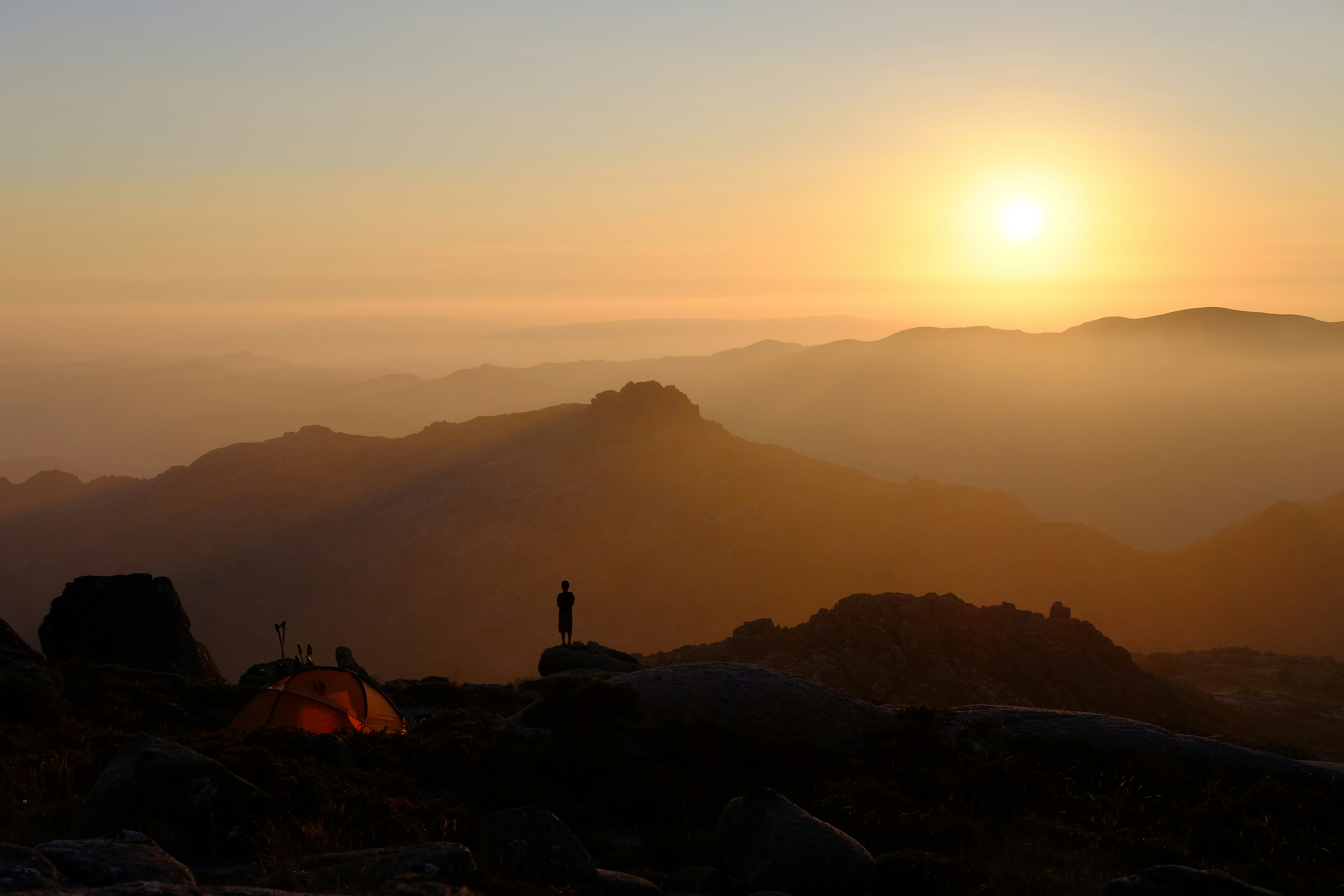 person standing on mountain near orange dome tent during sunrise