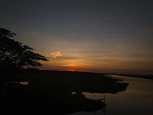 Tranquil sunset over a calm river with subtle Islamic architectural silhouettes.