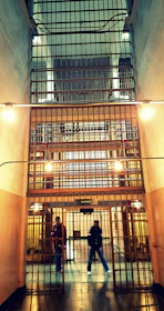 A tense confrontation between the officer and a prisoner, framed by cold metal bars and flickering lights.