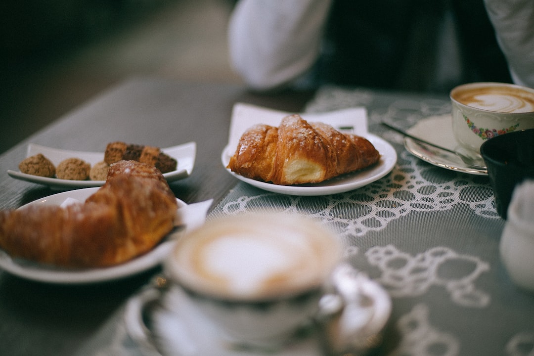 selective focus photography of croissant bread on white ceramic plate beside latte
