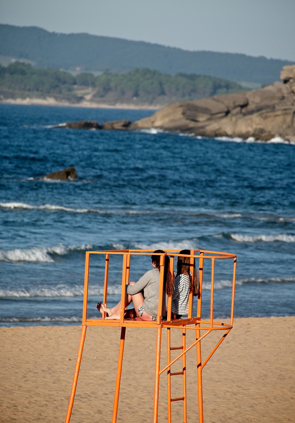 women sitting on metal frame in front of body of water