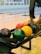 A selection of colorful bowling balls is seen in a bowling alley with someone's hands selecting a ball. The background shows multiple bowling lanes and a clear, smooth wooden floor.