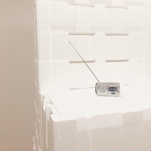 A small portable radio with an extended antenna is placed on top of stacked white styrofoam blocks. The setting appears minimalistic, with the radio being the focal point.